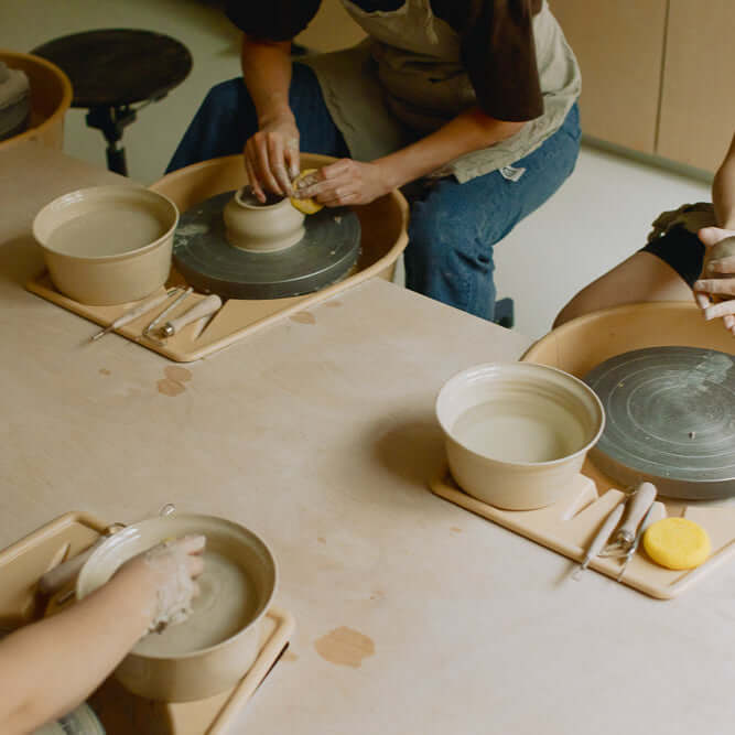 Group pottery class with participants using potter's wheels to create clay pieces, emphasizing hands-on learning.