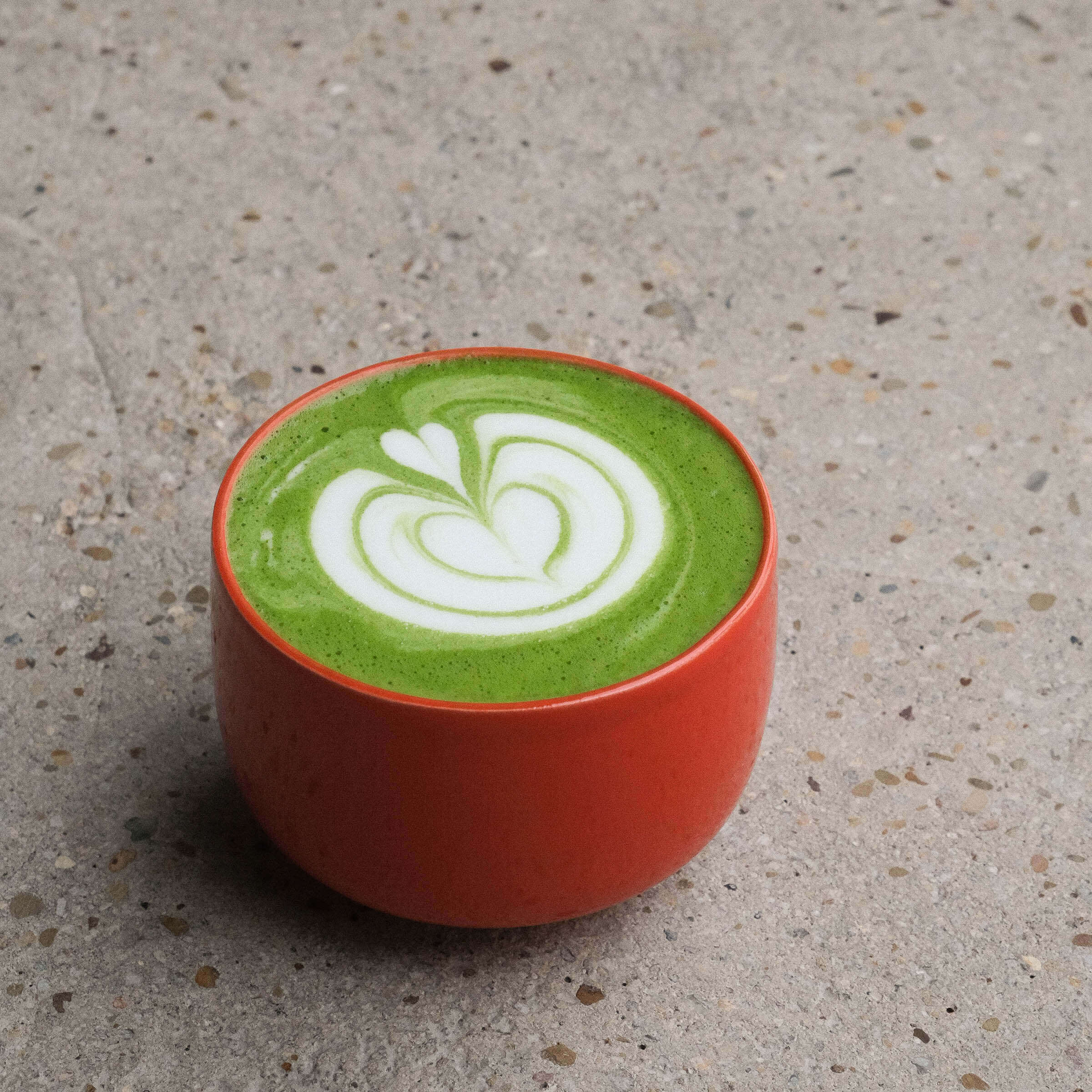 A vibrant green matcha drink served in a red cup, featuring beautiful latte art on top, showcasing Matcha Cups.