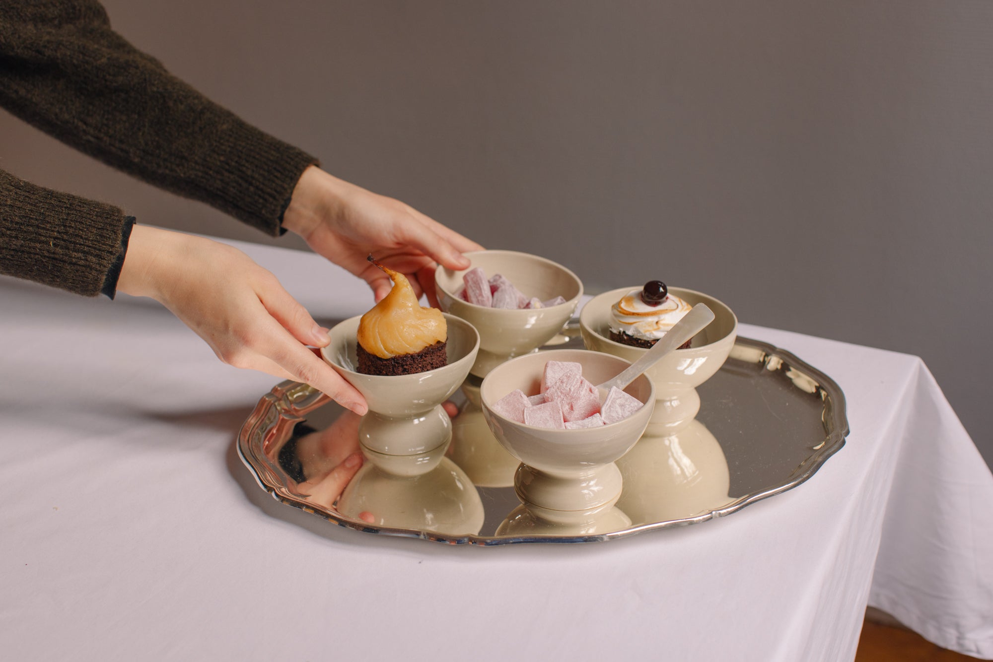 Hände, die handgemachte Keramikküchenutensilien mit Desserts präsentieren; Geschenke unter 50 €.