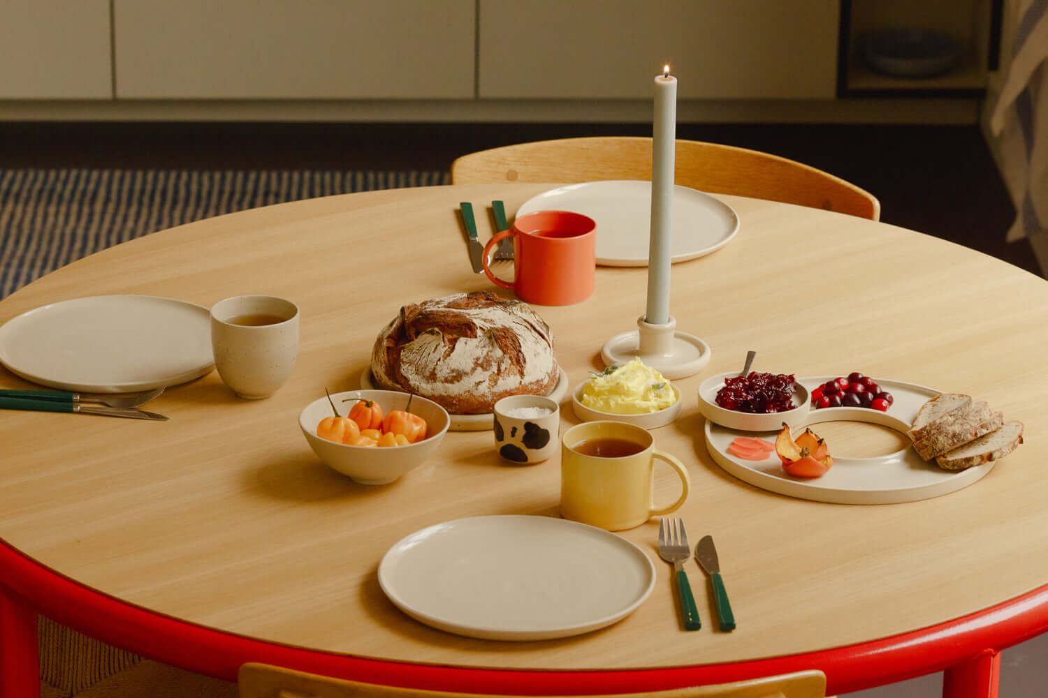 A cozy breakfast setup on a wooden table featuring bread, fruit, coffee, and a candle centerpiece.