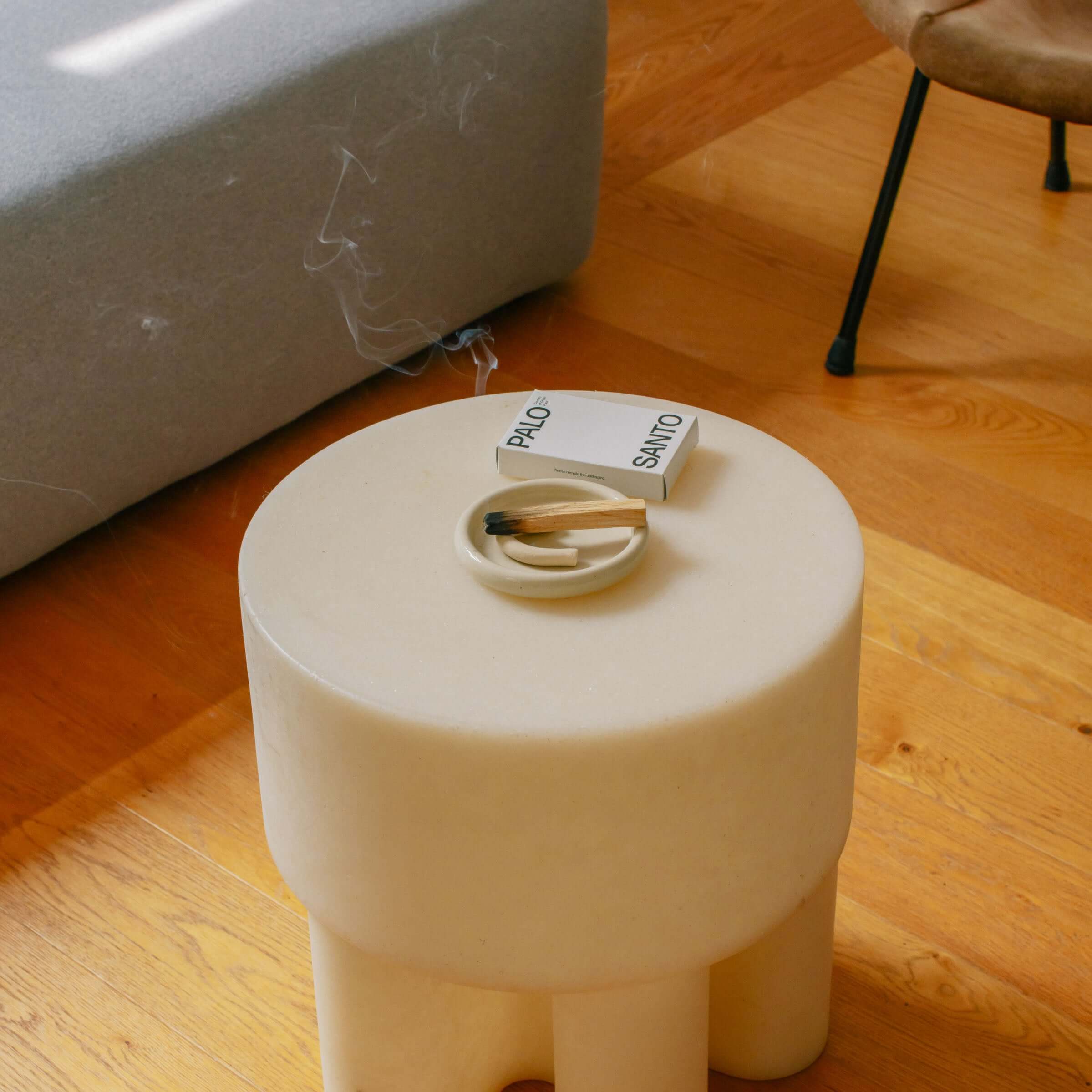 Palo Santo set displayed on a modern round table, featuring a dish and Palo Santo sticks on a tranquil wooden floor.