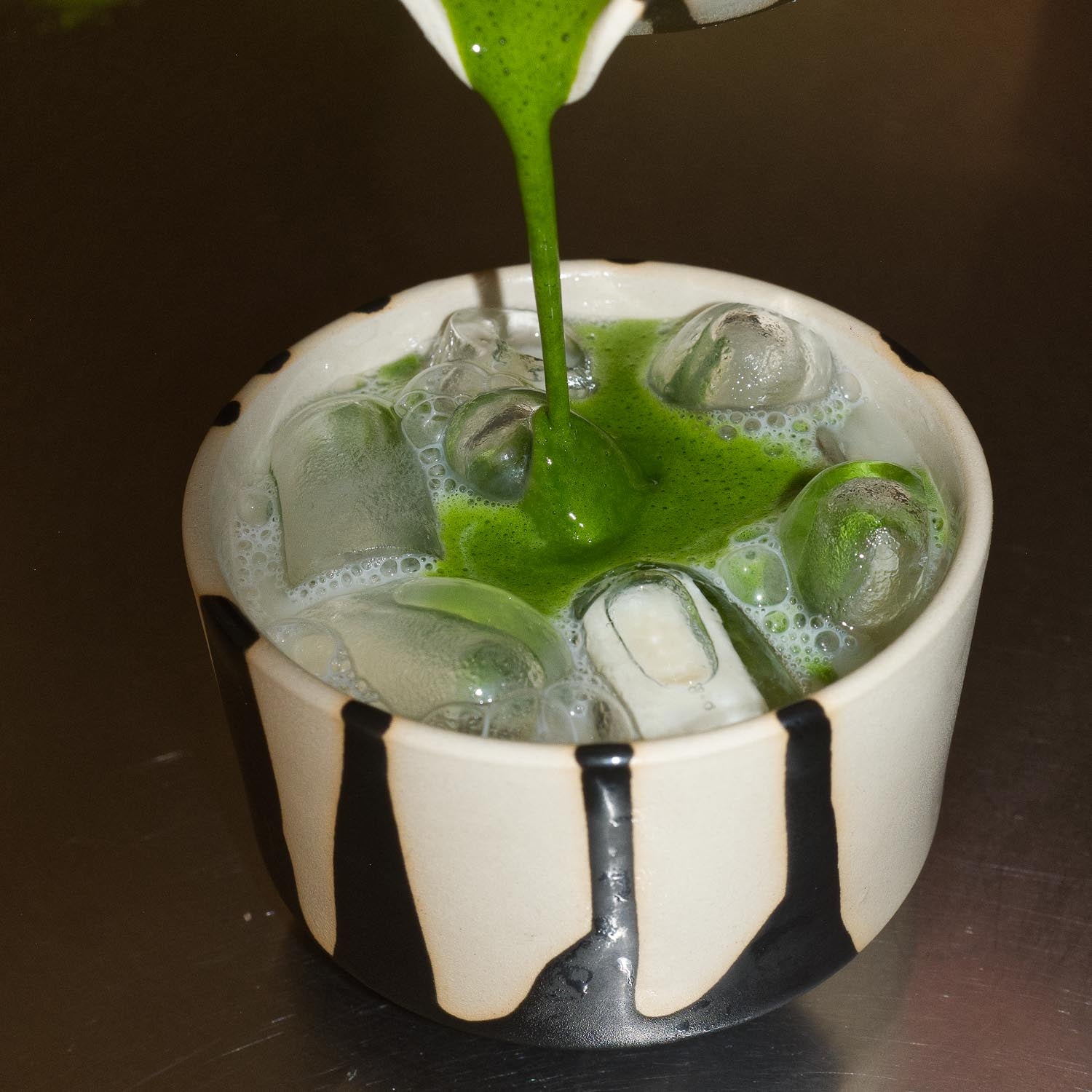 Matcha Set – Otis - Ceremonial Matcha: Grüner Matcha wird in eine dekorative Schale gegossen, umgeben von Eis.
