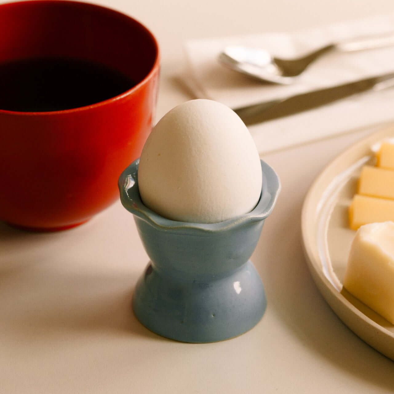 Handmade Stoneware Egg Cup – Egg Cup Iceblue mit einem weißen Ei, umgeben von Kaffee und Butter.