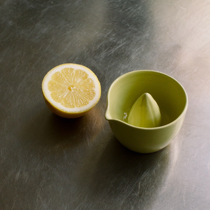 Handgemachte Zitronenpresse aus Steinzeug in Neon Gelb mit ausgepresster Zitrone.