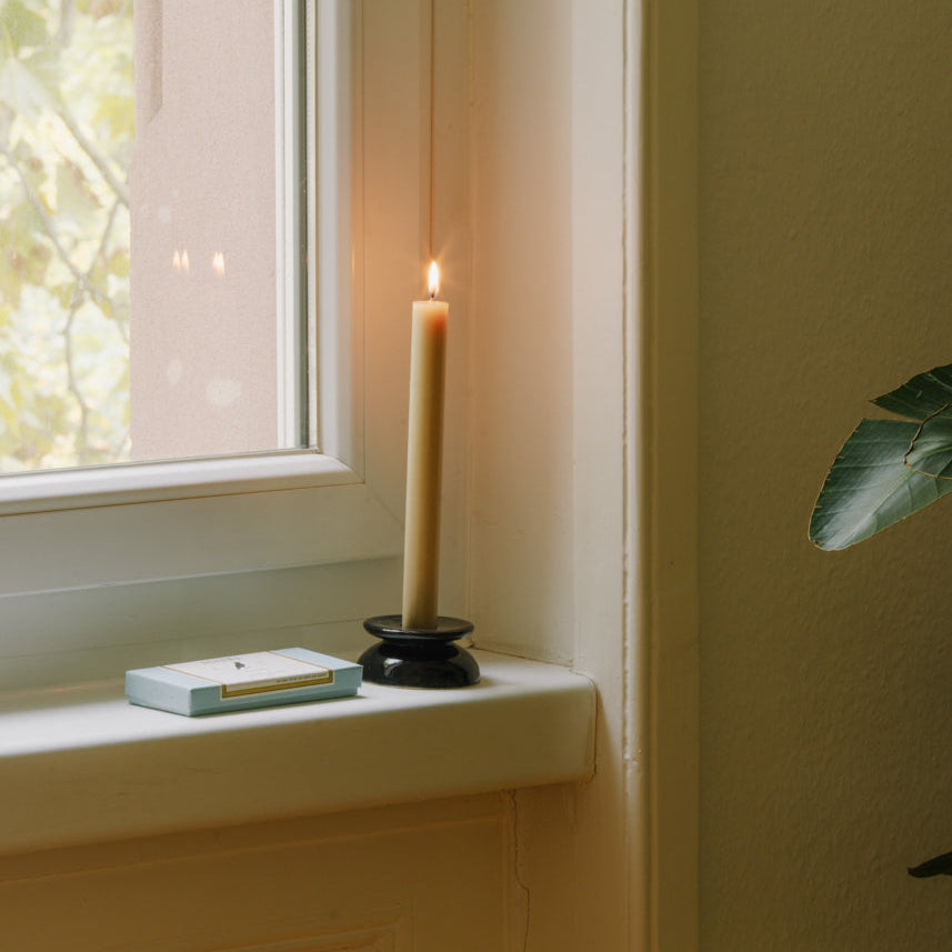 Candle Holder Black, low glossy black stoneware candle holder with a lit taper candle on a windowsill
