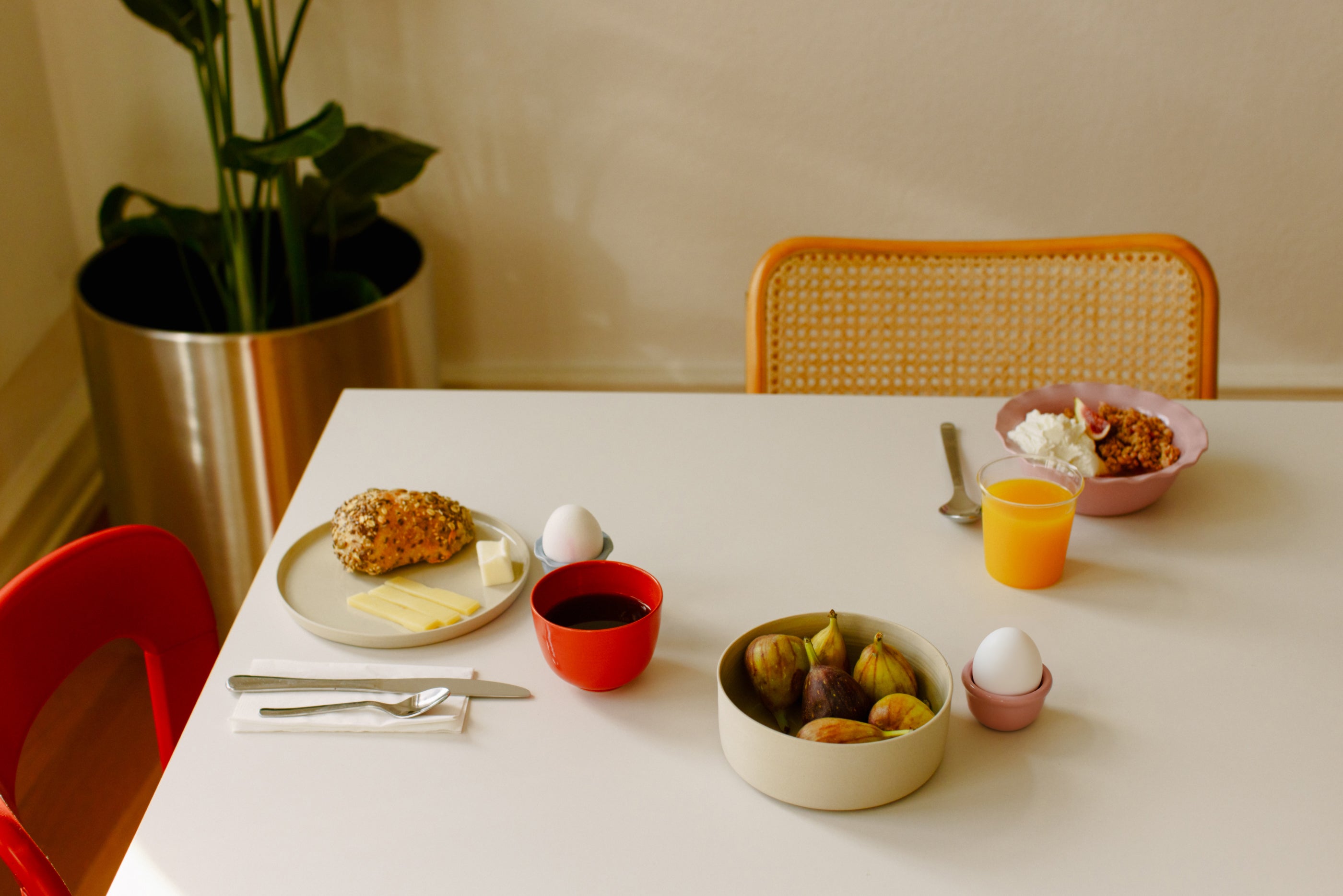 A cozy breakfast table with pastries, eggs, fruit, and drinks, surrounded by modern decor and plants.