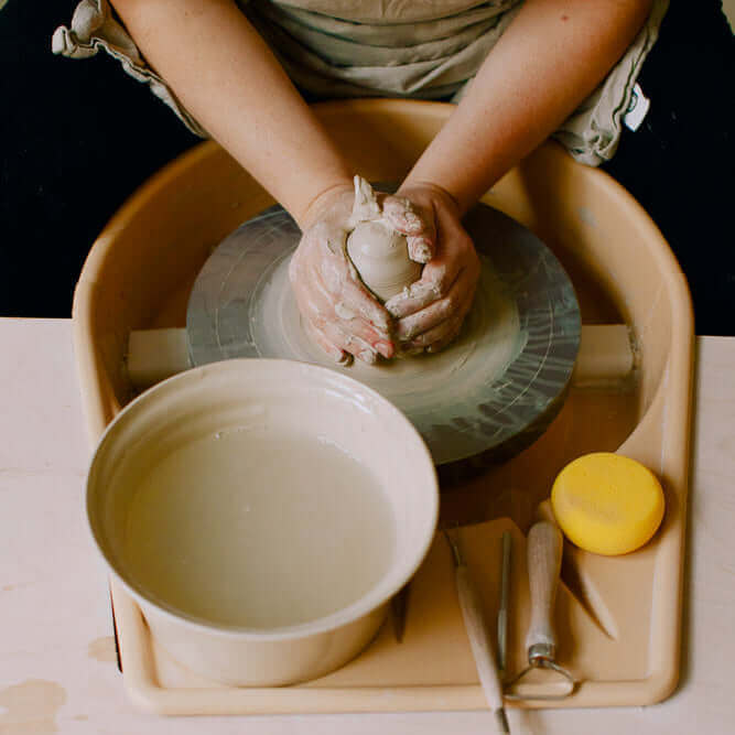 Töpferkurs für Einsteiger: Hände formen Ton auf einer Drehscheibe in der Keramikwerkstatt.