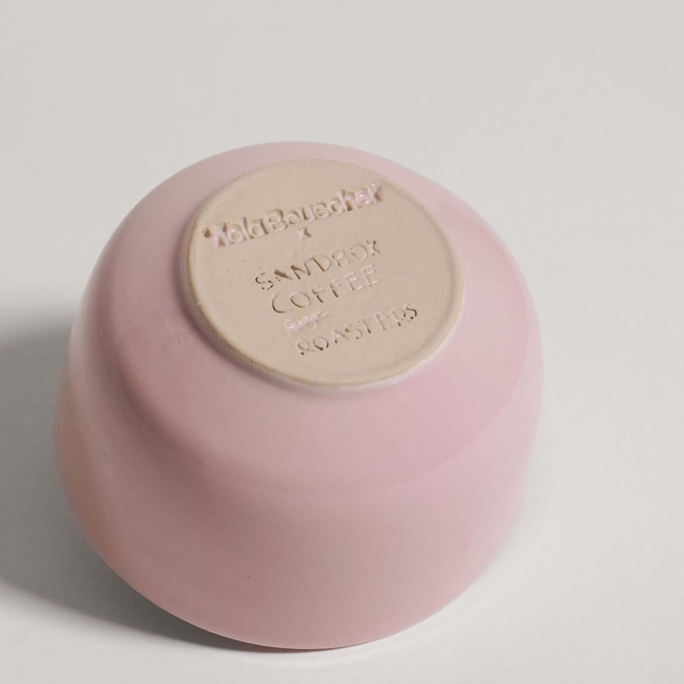 Handgemachter Rosa Kaffee Becher mit Sandbox Coffee Logo auf der Unterseite.