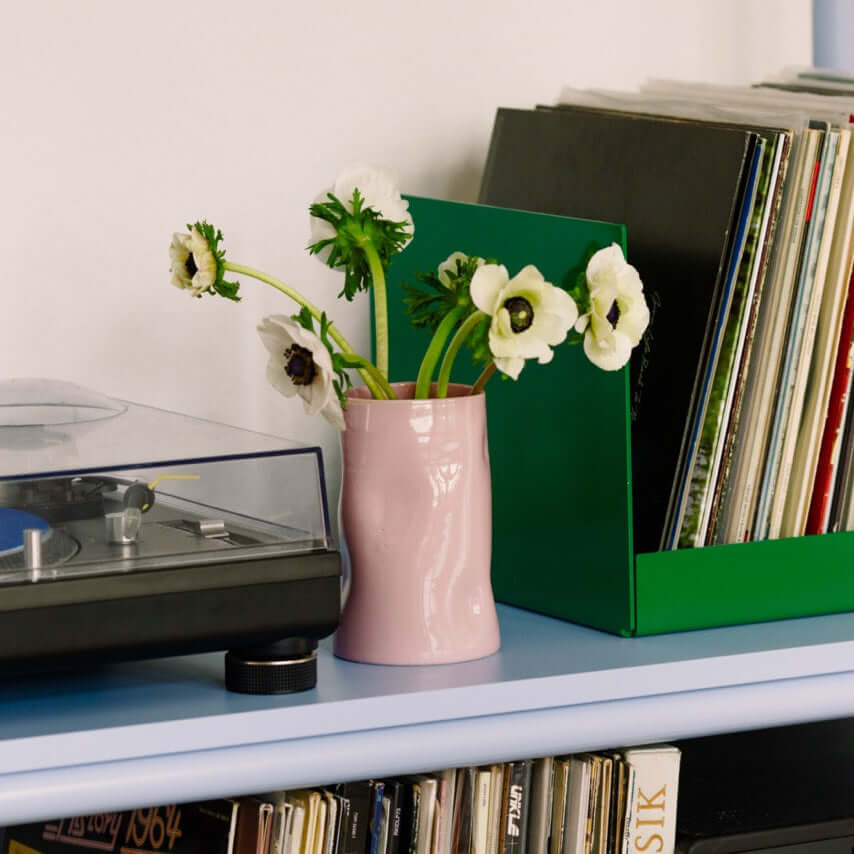 Handcrafted Pink Ceramic Vase – Vase Pink with flowers on a shelf next to a record player and green box.