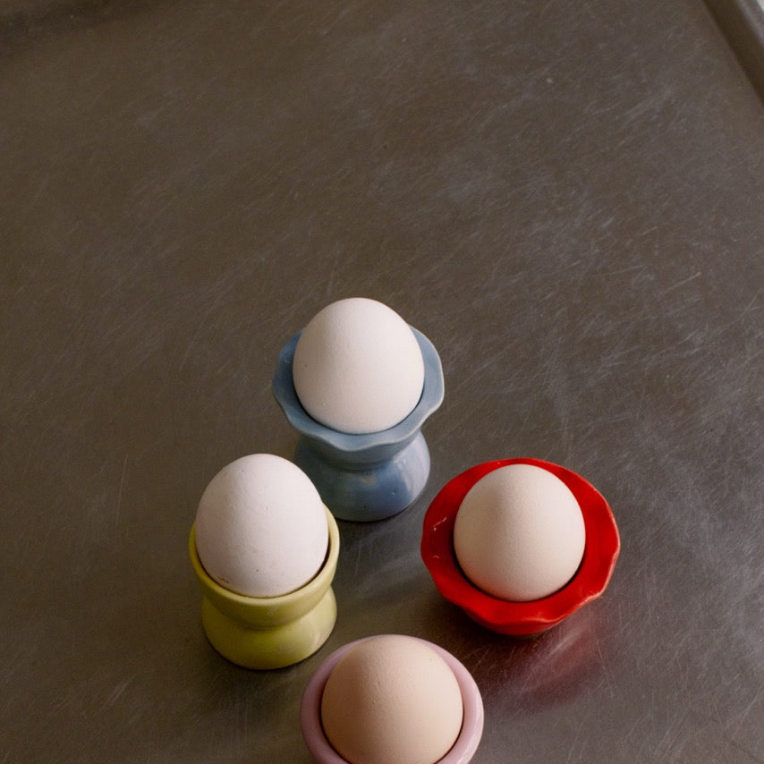 Handgemachter Eierbecher aus Steinzeug in verschiedenen Farben mit frischen Eiern.