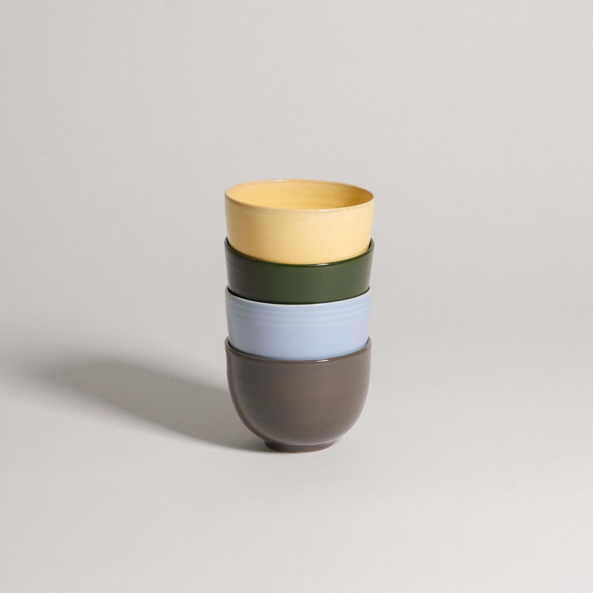 Colorful stack of cups from the Mix & Match - Cup & Mug Bundle, featuring yellow, green, blue, and brown.