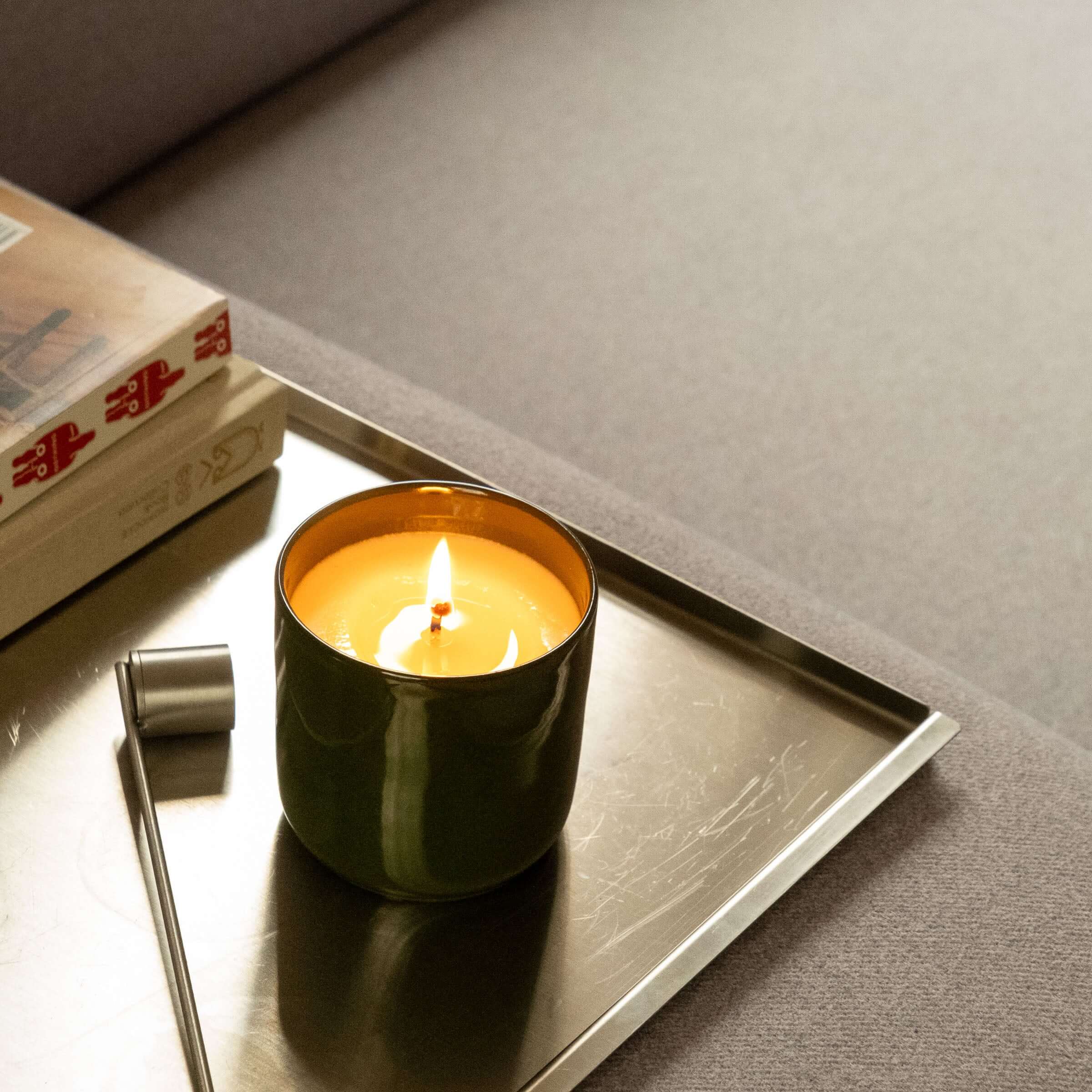 Duftkerze Zypresse in grünem Keramikbecher auf einem Tablett neben Büchern und einem Tisch.