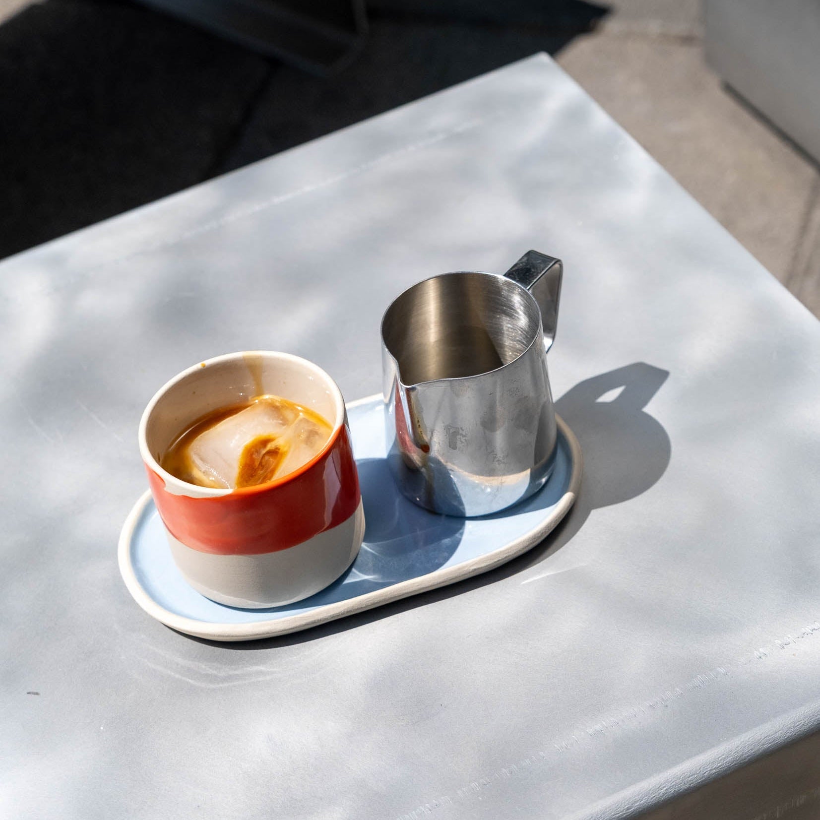 Serving Tray Oval Iceblue mit einer Tasse Kaffee und einem Milchkännchen auf einem Tisch.