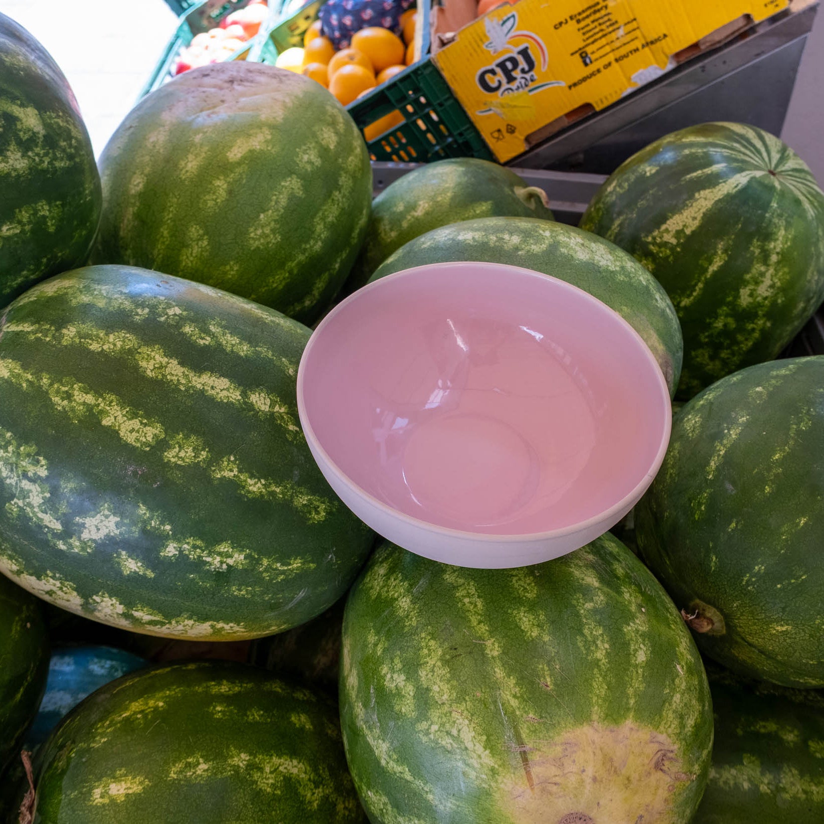 Servierschüssel Pink - Vorbestellung auf einem Berg von Wassermelonen, mit glänzendem pinken Innenleben.