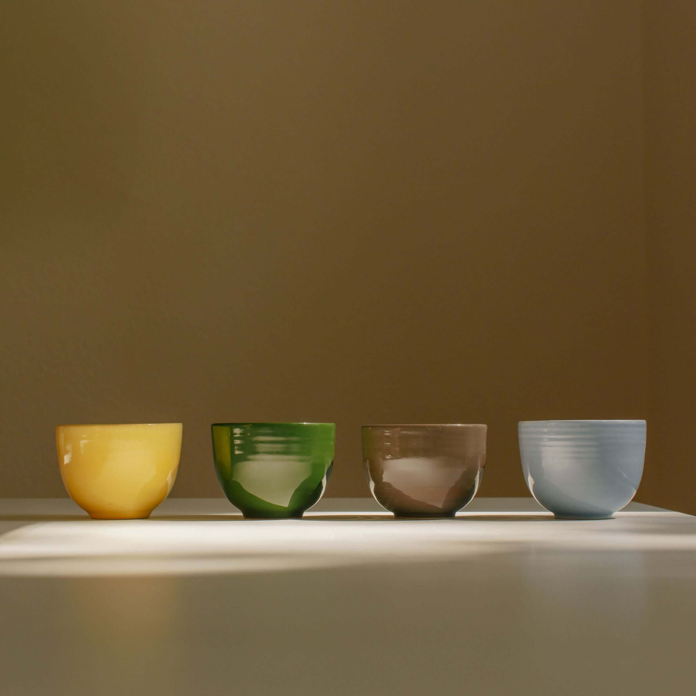 Set of 4 handcrafted stoneware coffee cups in yellow, green, brown, and ice blue, highlighting ceramic beauty.