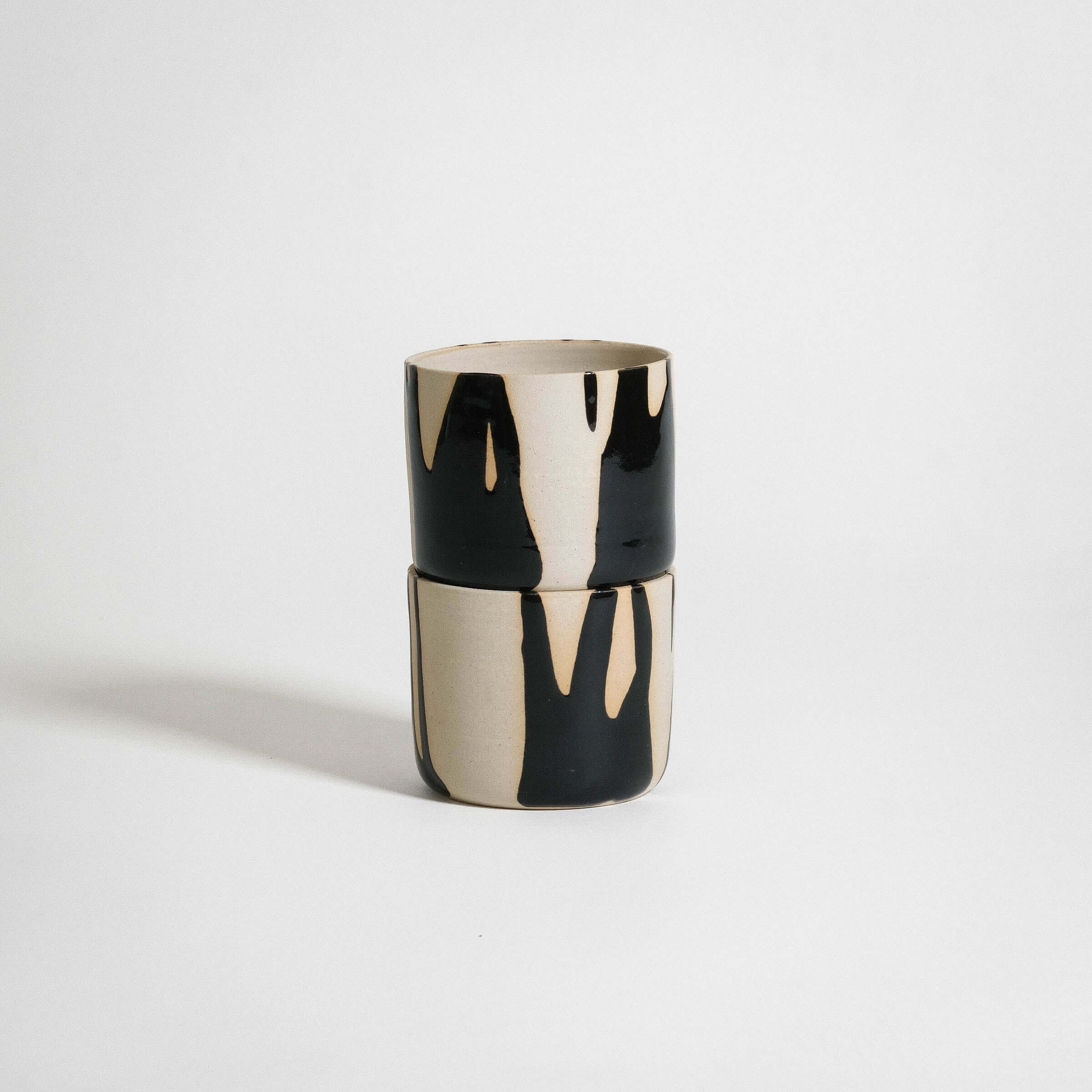 Handcrafted stoneware coffee cup in black and cream, featuring a glossy finish and natural clay texture, dishwasher-safe.