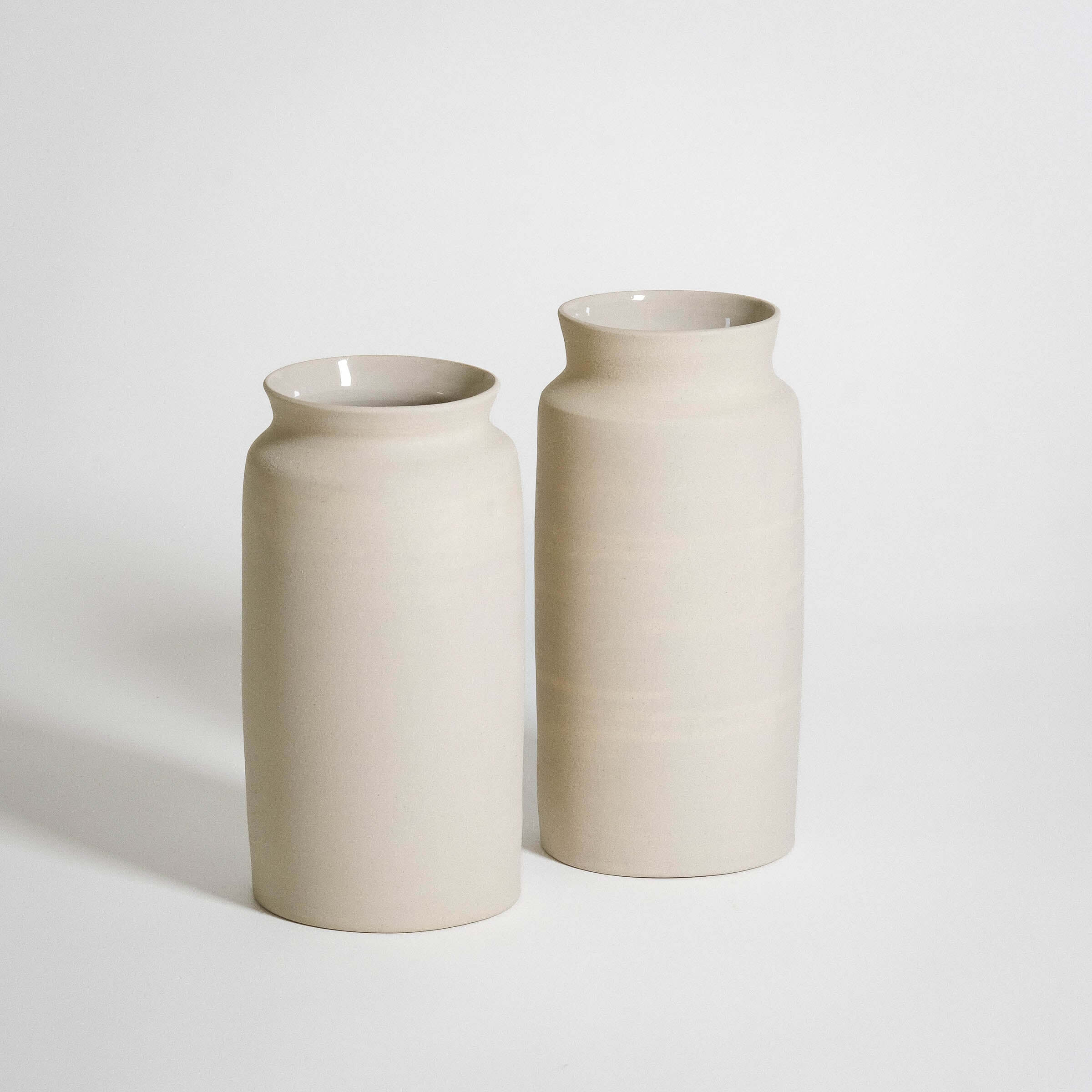 Two handmade ceramic vases in a soft, neutral color, perfect for displaying flowers or enhancing home decor.