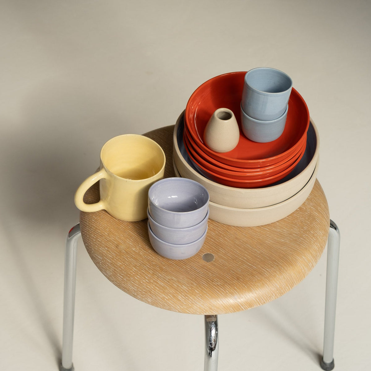 A coordinated ceramic tableware set arranged on a wooden stool.
