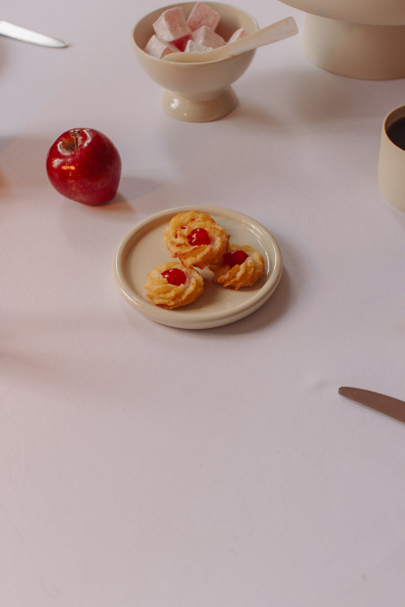 Handmade ceramic dishes displayed with bread, olives, pears, and dips on a white tablecloth.