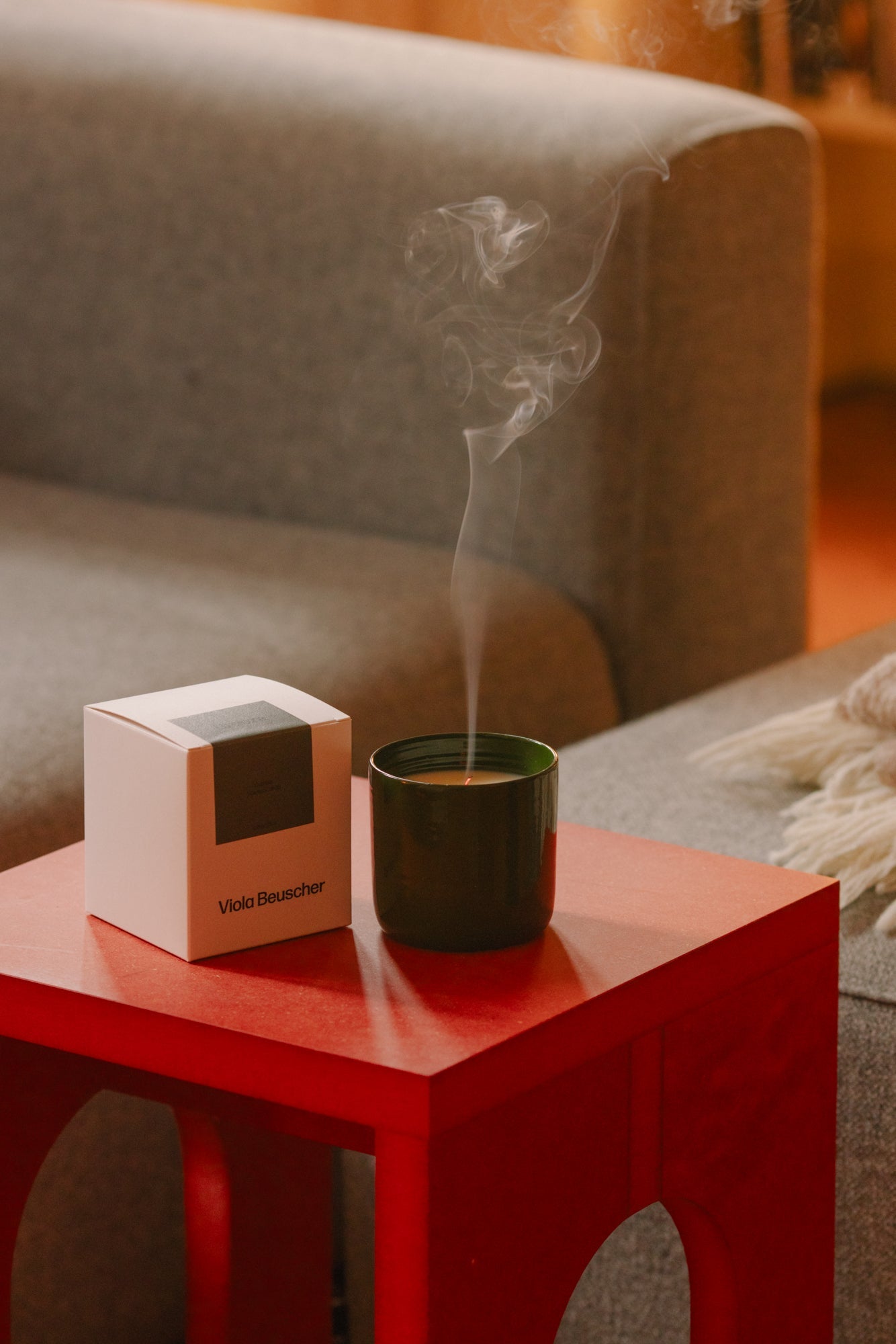 Herbstliche Duftkerzen auf einem Nachttisch, umgeben von einem gemütlichen Bett und einem Buch.