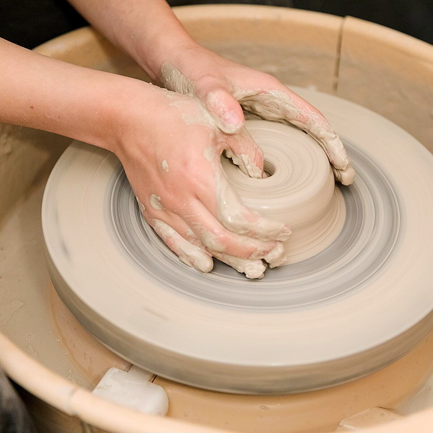 Hands shaping clay on a pottery wheel during a Beginner Wheel Class, showcasing the art of pottery creation.