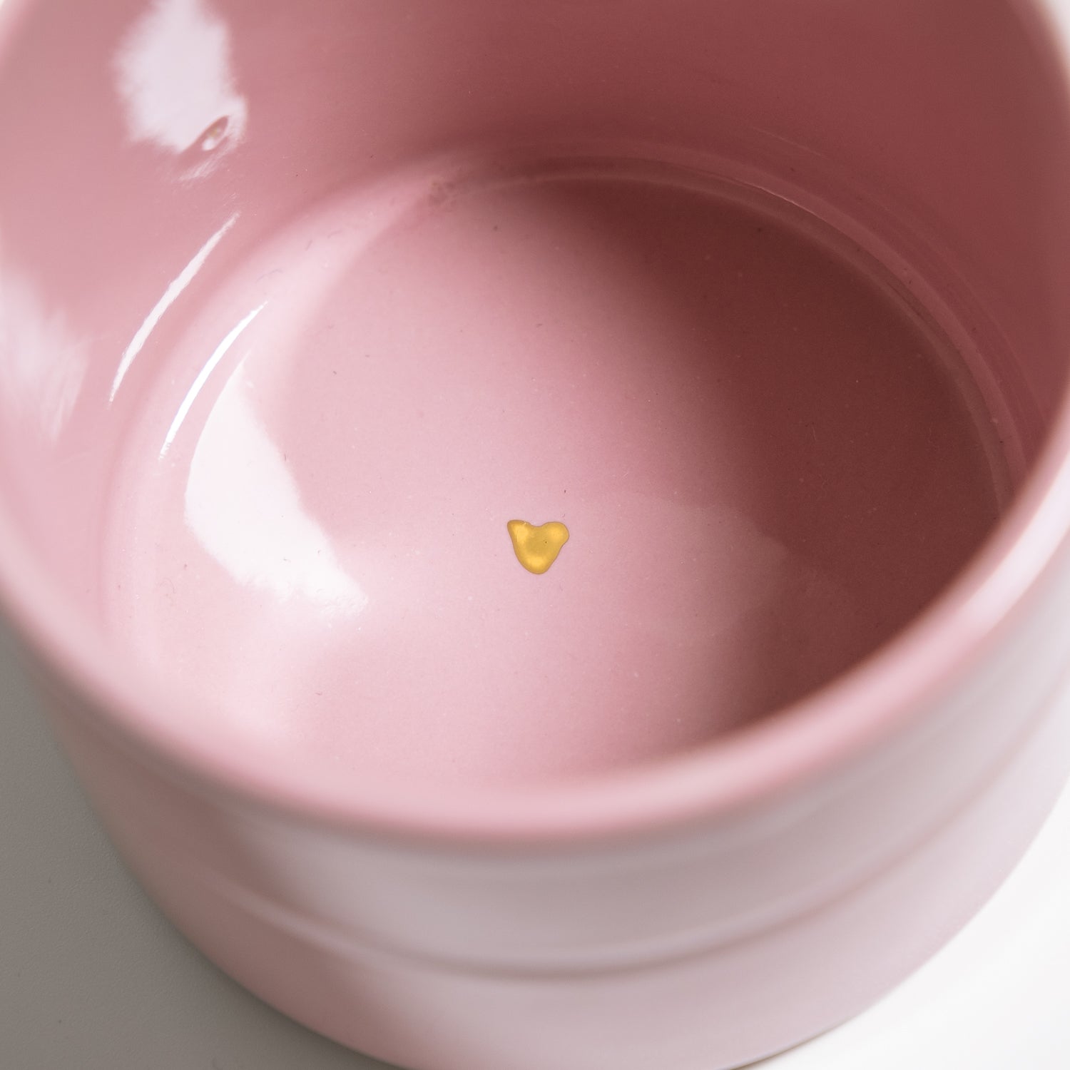 Handgemachter Keramik Kaffeebecher innen mit goldenen Herzdetail auf rosa Hintergrund.