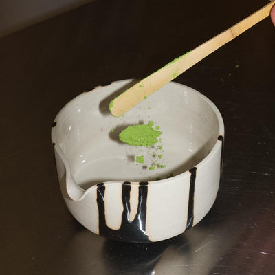 Matcha Pouring Bowl – Otis mit grünem Matcha-Pulver und Holzlöffel auf einer Metalloberfläche.