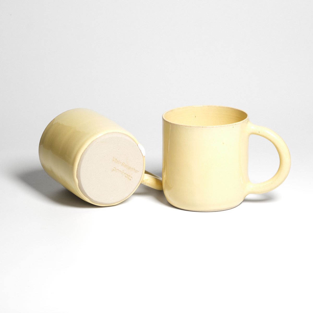Yellow Pankratiushof mug with handle – one mug on its side beside an upright mug.