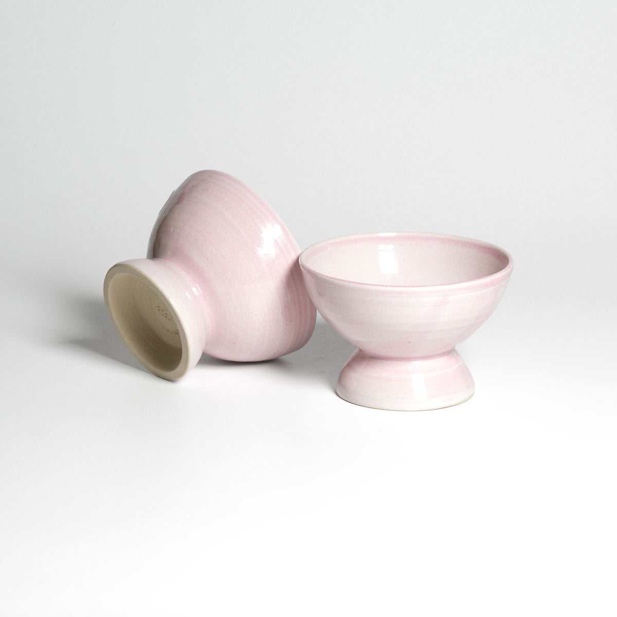 Roséfarbene Dessertschale auf kleinem Fuß – zwei Schalen, eine seitlich liegend.