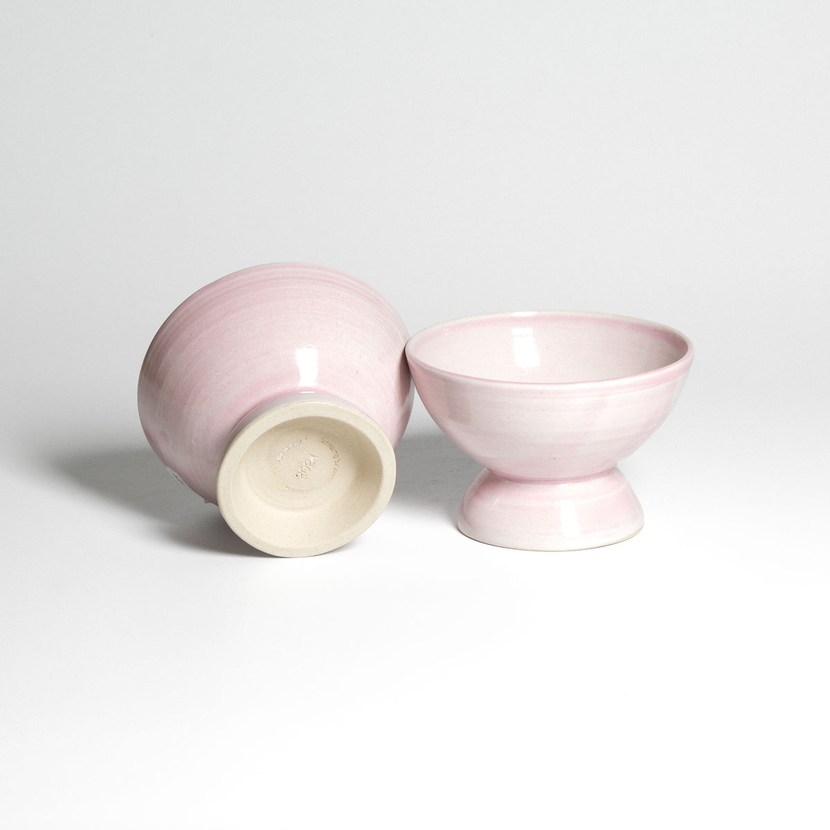 Roséfarbene Dessertschale auf kleinem Fuß – Unterseite neben aufrechter Schale.