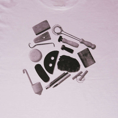 Arranged pottery tools graphic design on a lilac t-shirt, featuring various pottery implements.