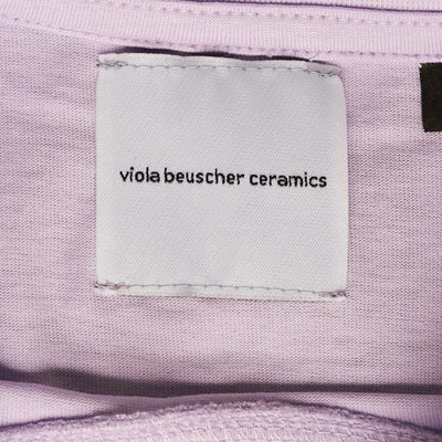 Label showing "viola beuscher ceramics" on lilac T-shirt fabric.