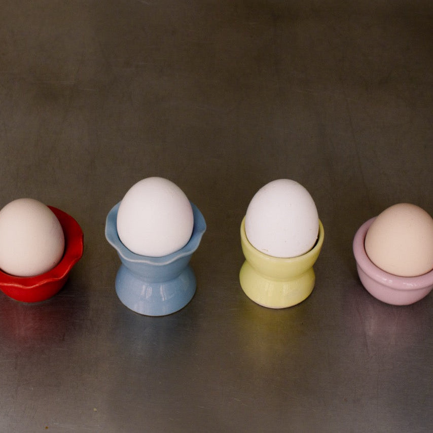 Handgemachter Eierbecher aus Steinzeug in Neon Gelb und anderen Farben mit Eiern darauf.