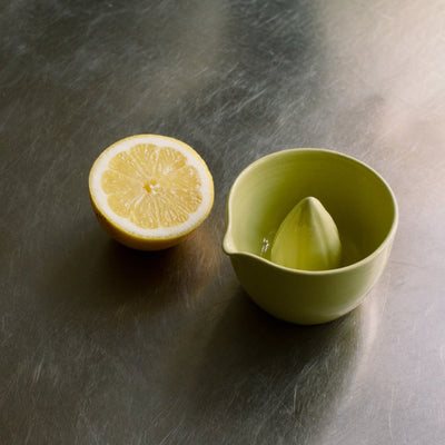 Handgemachte Zitronenpresse aus Steinzeug in Neon Gelb mit ausgepresster Zitrone.
