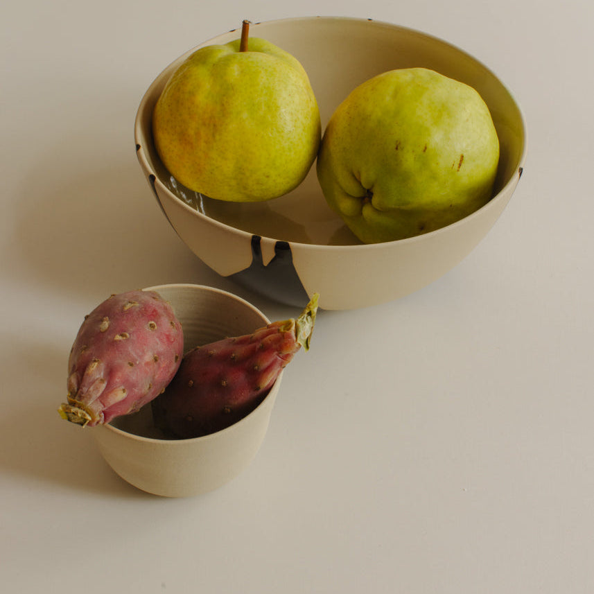 Two beige ceramic bowls on a light neutral background, one holding two green pears and the other holding two red sweet potatoes.