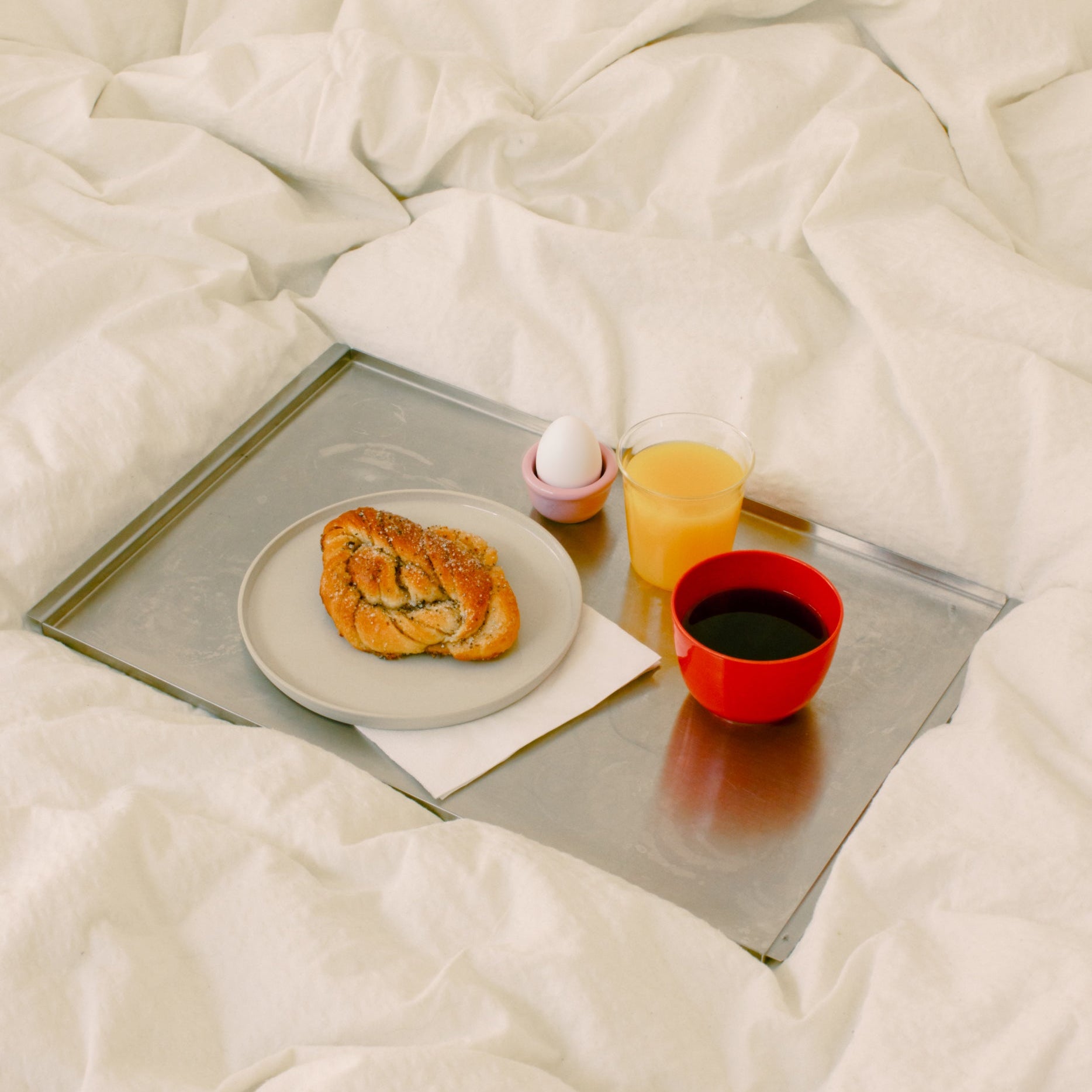 Handgemachtes Geschirr Set auf einem Tablett mit Brötchen, Orangensaft, Kaffee und einem Eierbecher.