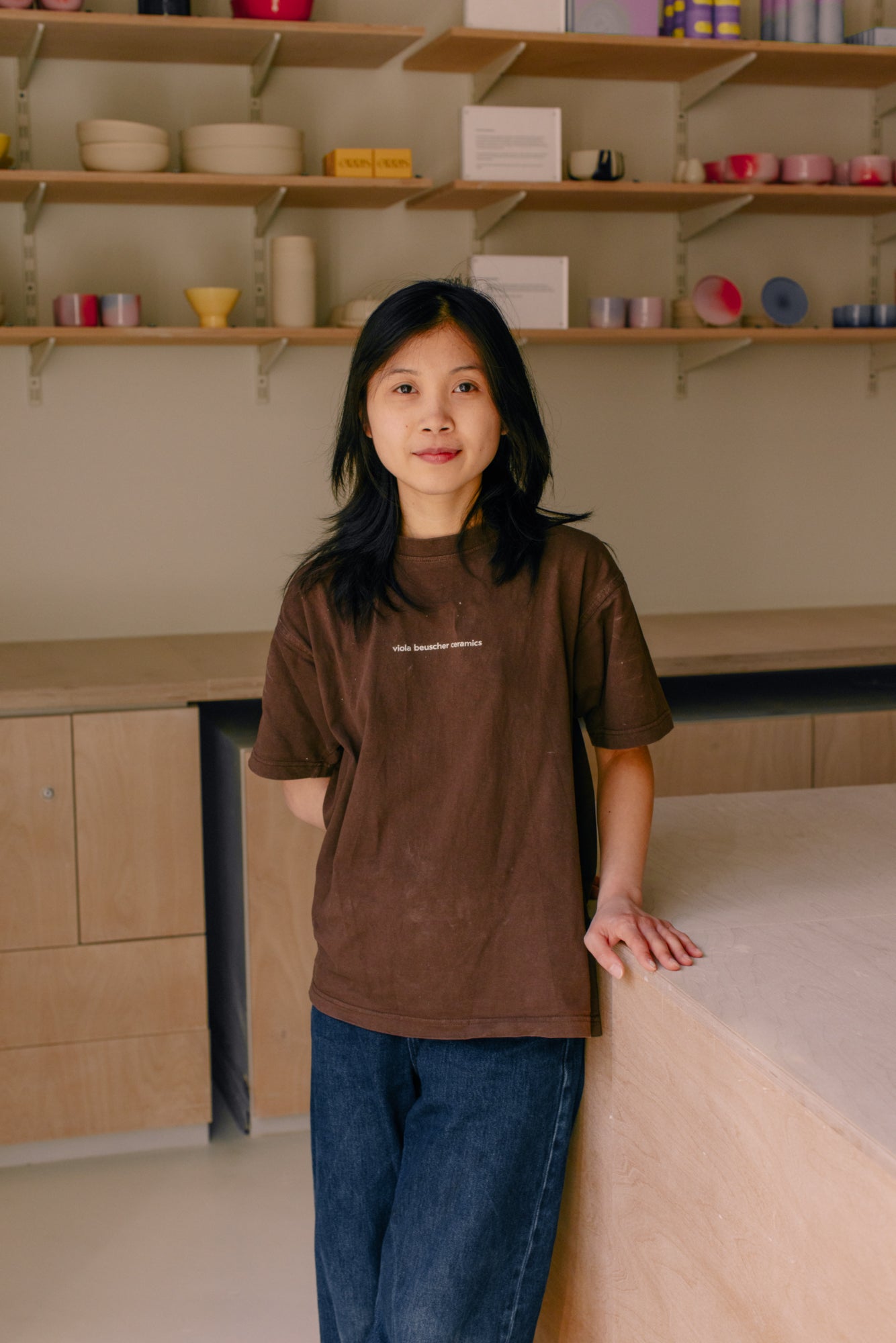 Ein junges Mädchen in einem braunen T-Shirt steht an einem Tisch in einem modern gestalteten Raum.