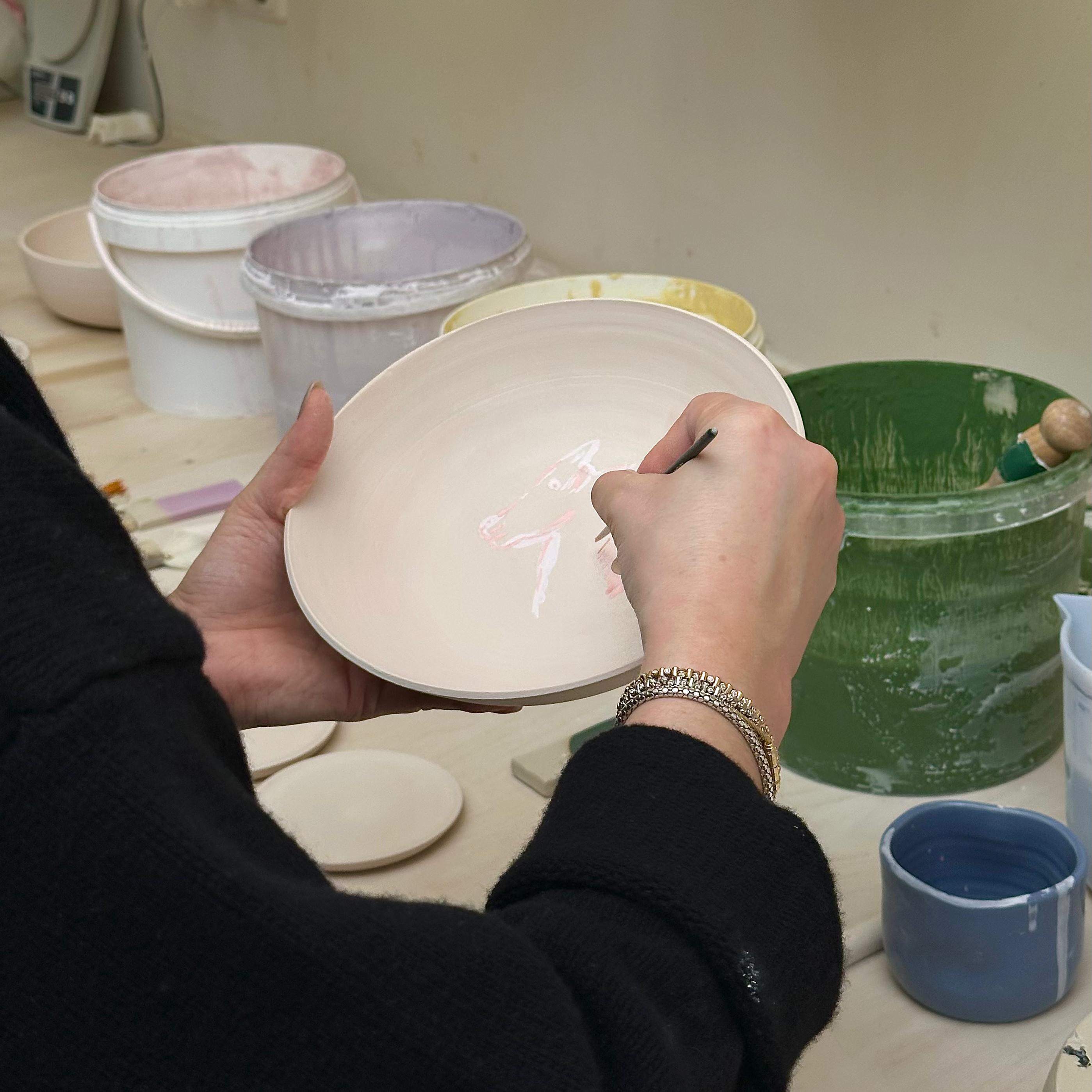 Teilnehmerin beim Glasur Workshop Frankfurt malt auf einer Keramiktellerfläche.