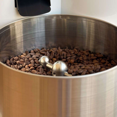 Röstkaffee in einem großen, silbernen Behälter mit einem Edelstahl-Rührwerkzeug für perfekten Genuss.