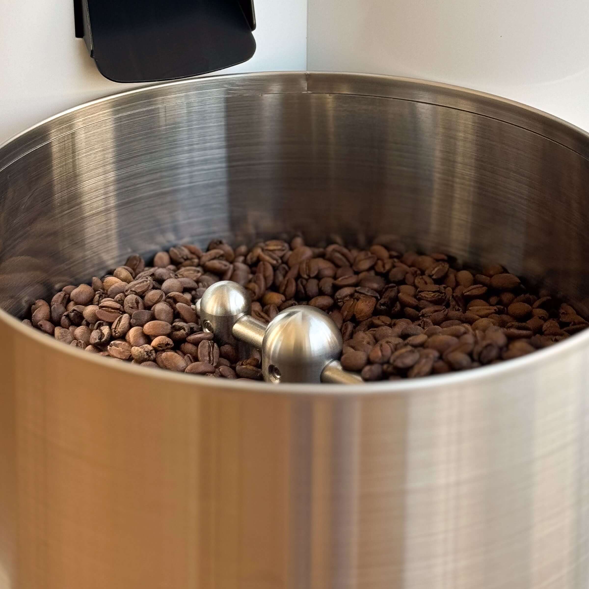 Röstkaffee in einem großen, silbernen Behälter mit einem Edelstahl-Rührwerkzeug für perfekten Genuss.