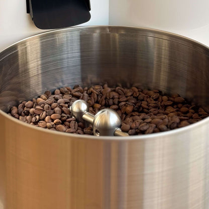 Röstkaffee in einem großen, silbernen Behälter mit einem Edelstahl-Rührwerkzeug für perfekten Genuss.