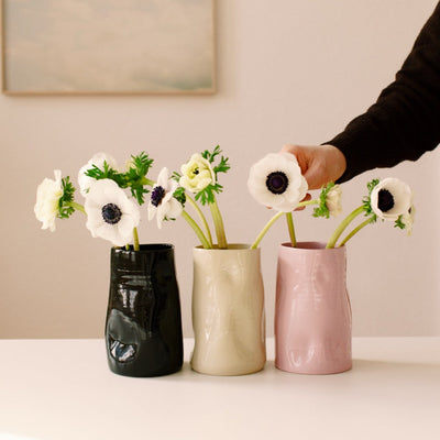 Three vases with flowers on a light surface, with a hand reaching towards one of them.