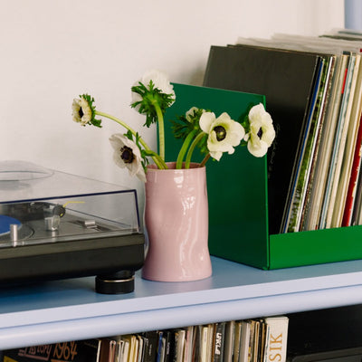 Handgefertigte rosa Keramikvase mit Blumen auf einem Regal, umgeben von Schallplatten und einem Plattenspieler.