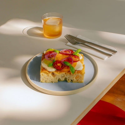 Handcrafted iceblue dinner plate featuring a colorful vegetable dish, set on a modern table with a refreshing drink.