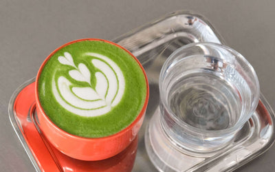 Matcha Set – Classic - Organic Ceremonial Matcha Supreme displayed with latte art in an orange cup and a glass of water.