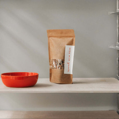 Miso-Miso-Granola - Gesalzenes Karamell & Umami in der Verpackung mit einer roten Schüssel im Hintergrund, miso karamell granola mit umami.