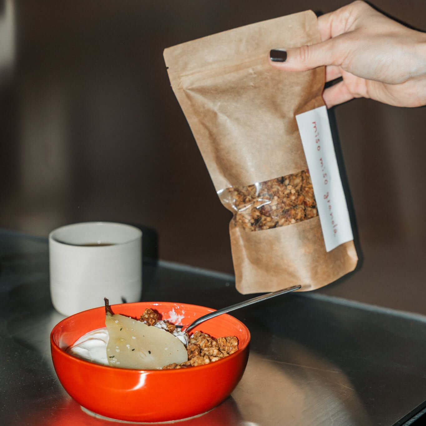 miso karamell granola mit umami in einer roten Schüssel, serviert mit Joghurt und einer Tüte Granola daneben.