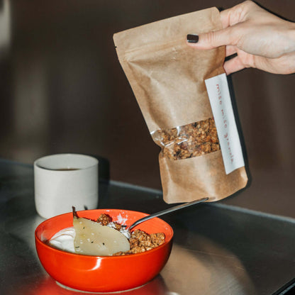 miso karamell granola mit umami in einer roten Schüssel, serviert mit Joghurt und einer Tüte Granola daneben.