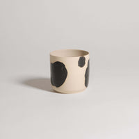 Handcrafted stoneware cup with black brush strokes, showcasing a unique design and glossy finish.