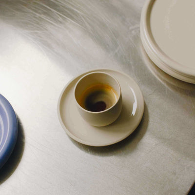 Set of 4 Nomi Creme espresso cups in grey stoneware with glossy glaze, featured on a metal surface.